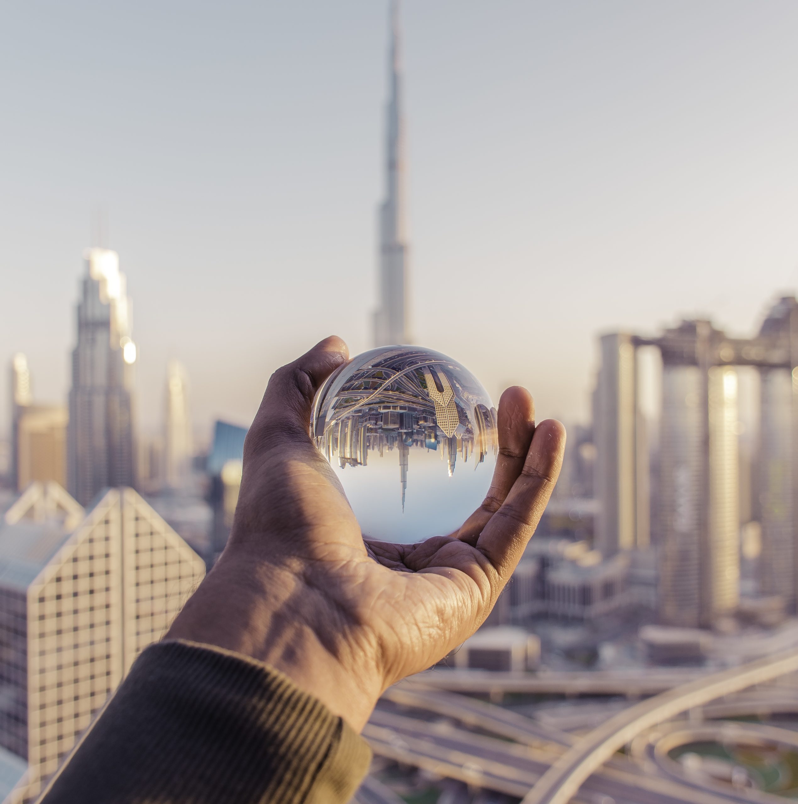 Closeup shot of a male hand holding a crystal ball with the reflection of the city architect-designed house